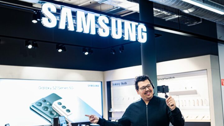 lachende promotor in een zwart vast met bril laat zijn telefoon Galaxy afdeling zien via facetimen op smartphone