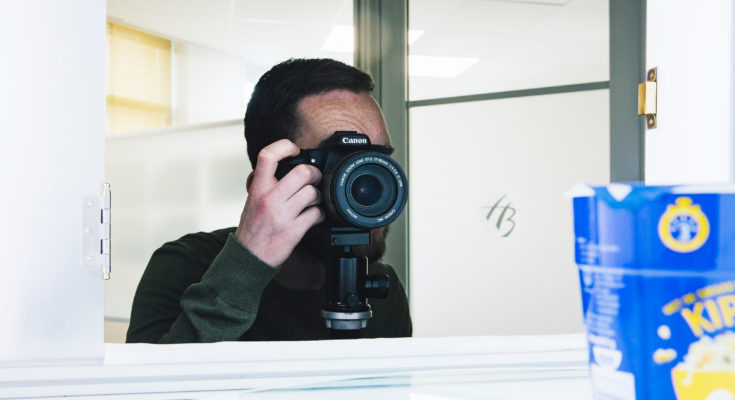 een bruinharige man maakt een foto met zijn Cancon cameratoestel op het kantoor van hamilton bright trademarketing