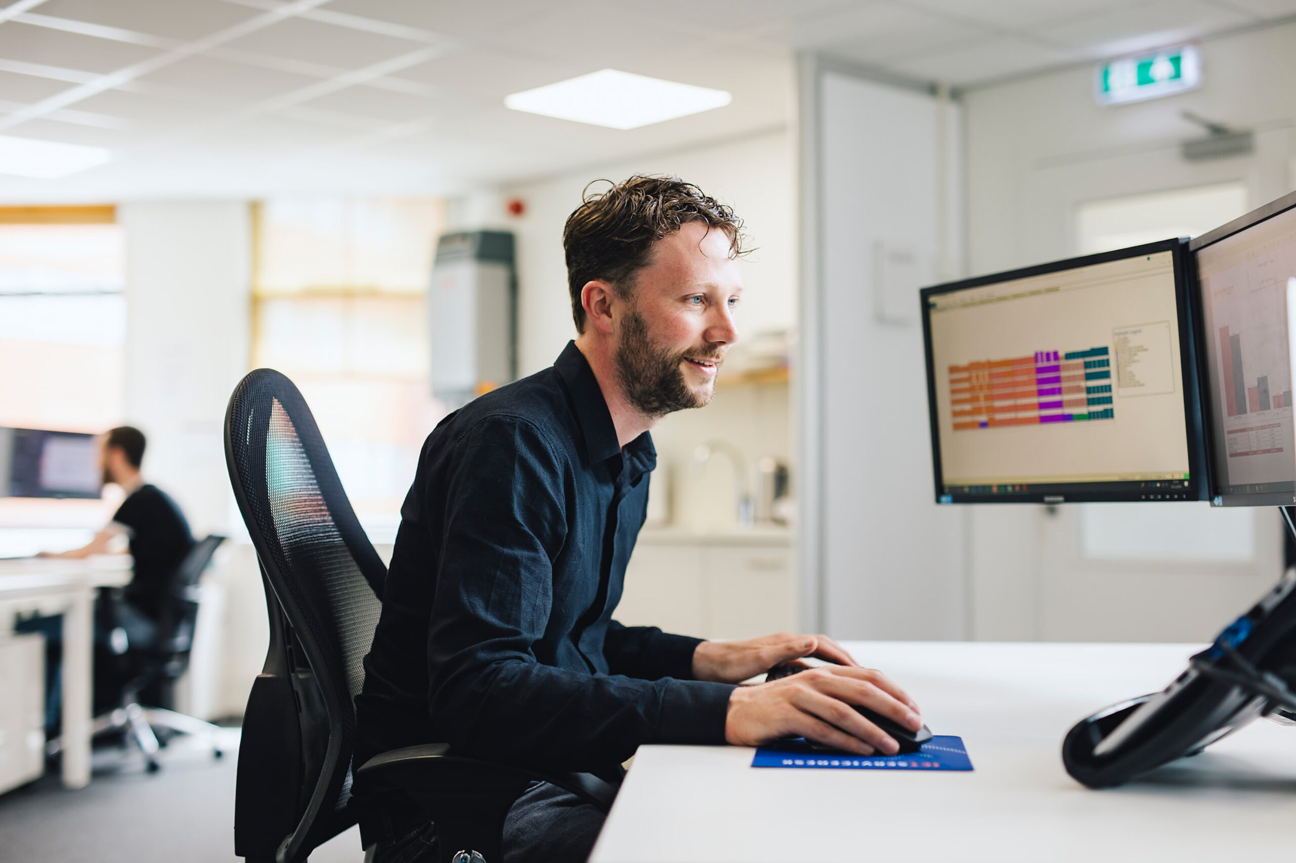 kantoormedewerker met baardje zoekt op zijn computer in een kantoorpand