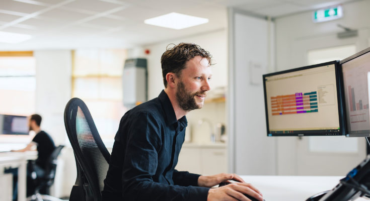 kantoormedewerker met baardje zoekt op zijn computer in een kantoorpand