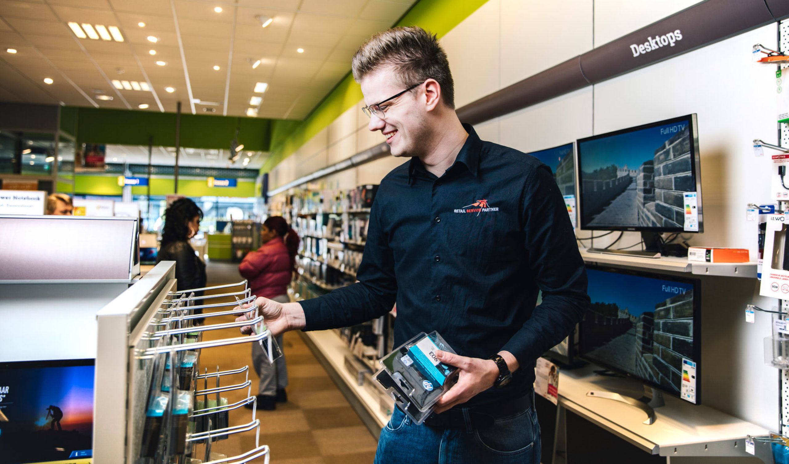 een service merchandiser vult het cartridges schap van de MediaMarkt bij