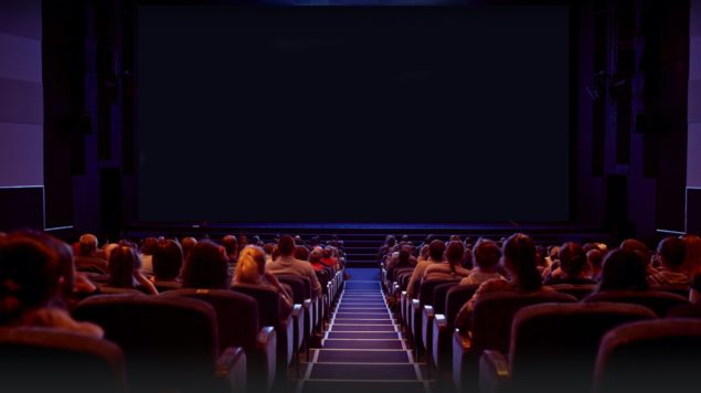 een donkere bioscoopzaal met veel publiek in de bioscoopstoelen
