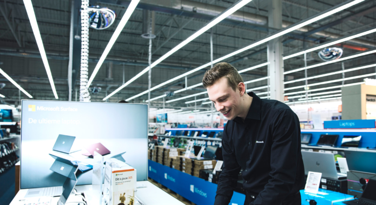 Microsoft verkoper zoekt iets op via zijn laptop in de MediaMarkt